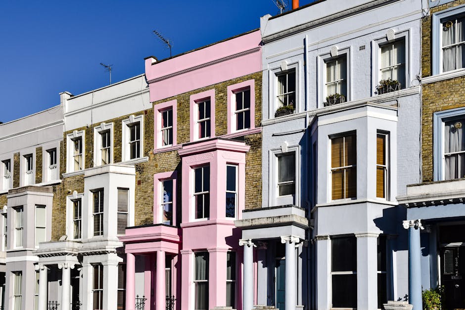 A row of three-storey Victorian terraced houses in a residential street, featuring a white house with blue window frames and a red house with black window trims. The red house has a brick staircase wi