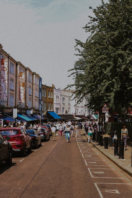 A street scene on Lancaster Road in Notting Hill shows rows of white, historic-style terraced buildings with ornate balconies and large windows lining both sides of the road. Several vehicles are park