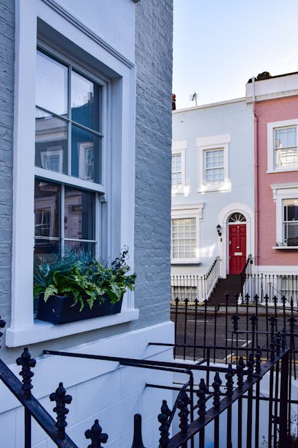 The image shows a row of colourful Victorian terraced houses with detailed architectural features, including large bay windows, decorative cornices, and ornate wooden trims. The houses are painted in